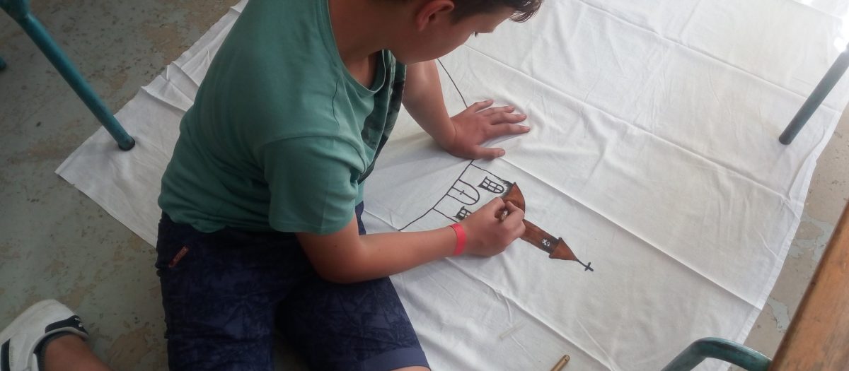 enfant qui dessine une église sur une grande feuille blanche, au sol